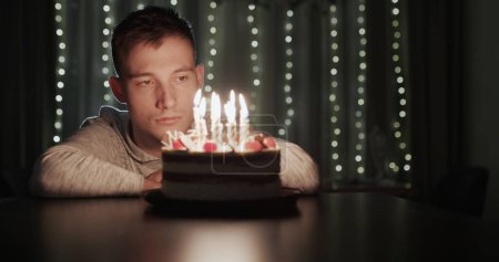 Foto de Joven triste mirando pastel de cumpleaños con velas solo. - Imagen libre de derechos