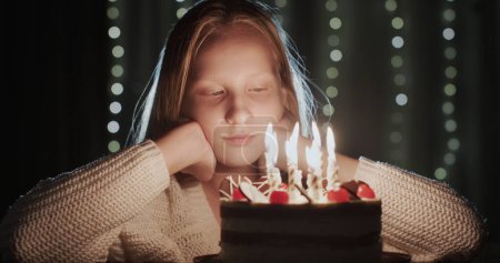 Téléchargez les photos : Une adolescente légèrement triste regarde les bougies sur son gâteau d'anniversaire. - en image libre de droit