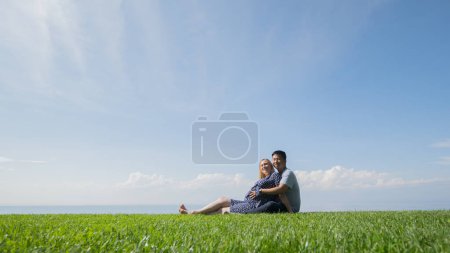 Photo for Multi-ethnic couple resting on the green grass, admiring the beautiful nature. - Royalty Free Image