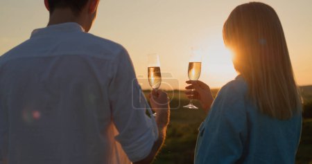 Photo for Young couple with glasses of red wine watching the sunset over a picturesque valley. - Royalty Free Image