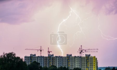 Téléchargez les photos : Un immeuble avec des grues de construction sur le fond du ciel nocturne où vous pouvez voir la foudre. - en image libre de droit