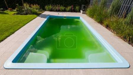Téléchargez les photos : Eau verte dans une piscine de la maison dans la cour d'une maison. Floraison due à une dose incorrecte de produits chimiques. - en image libre de droit
