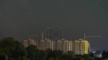 Foto de Silueta de un edificio residencial de varios pisos. Hay un cielo estrellado encima de él, grúas son visibles detrás de él. - Imagen libre de derechos