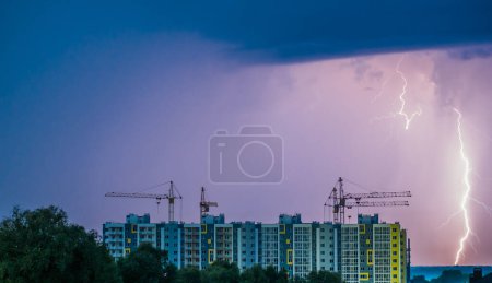 Foto de Un edificio de apartamentos con grúas de construcción sobre el fondo del cielo nocturno donde se puede ver un rayo. - Imagen libre de derechos