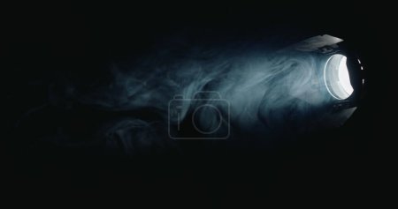 Téléchargez les photos : Une puissante source de lumière directionnelle brille dans l'obscurité, le brouillard tourbillonne dans le faisceau de lumière. - en image libre de droit