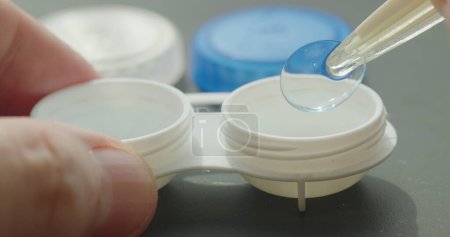 Close-up of contact lens container with tweezers in hand retrieving a lens.