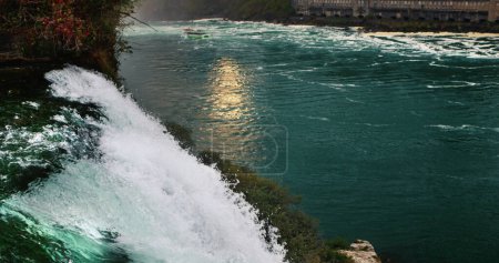 Abend an den Niagara Falls. Der Fluss reflektiert die untergehende Sonne, im Vordergrund ein mächtiger Wasserstrom.