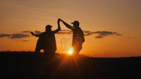 Photo for Two farmers dance merrily in a field. Silhouettes against the sky where the sun sets. - Royalty Free Image