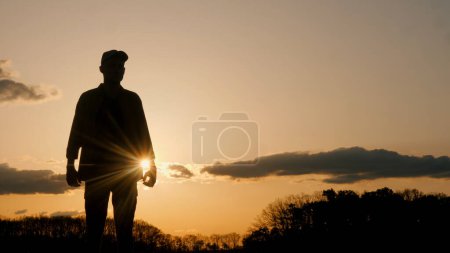 Foto de Silueta de un hombre pacíficamente de pie frente a una puesta de sol impresionante, rodeado por el cielo colorido y las nubes, mostrando un gesto alegre en armonía con la naturaleza - Imagen libre de derechos