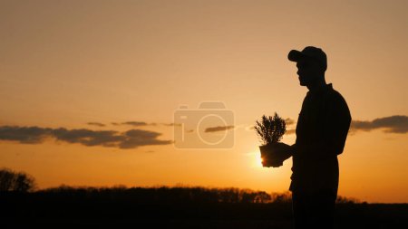 Foto de Un hombre sosteniendo un ramo de flores está de pie en silueta contra el cielo vibrante puesta de sol, rodeado de hierba y el horizonte pacífico - Imagen libre de derechos