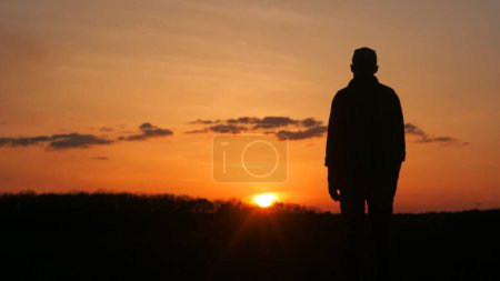 Téléchargez les photos : Une silhouette mans est vue contre le ciel rouge au coucher du soleil, debout devant une belle lueur secondaire avec des arbres et des nuages en arrière-plan - en image libre de droit