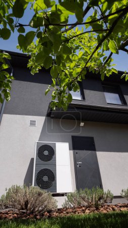 The wall of a modern cottage hosts the outdoor unit of a heat pump. High quality photo
