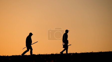 Foto de Dos hombres granjeros cruzan el campo llevando equipo de trabajo. Foto de alta calidad - Imagen libre de derechos