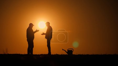 Téléchargez les photos : Silhouettes de deux fermiers serrant la main sur la toile de fond du coucher de soleil sur un champ. Photo de haute qualité - en image libre de droit