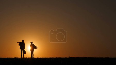 Silhouettes de deux agriculteurs homme et femme dans un champ où le soleil se couche.