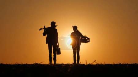 Au coucher du soleil, les silhouettes d'un agriculteur masculin et d'une agricultrice sont visibles dans le champ.