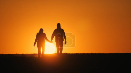 Téléchargez les photos : Silhouettes d'un jeune couple marchant côte à côte vers un coucher de soleil pittoresque. - en image libre de droit