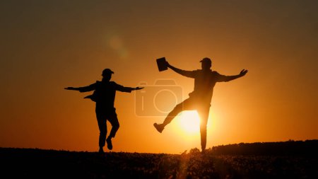 Silhouettes de deux hommes d'affaires dansant une danse joyeuse au coucher du soleil. Homme tenant un comprimé dans sa main. 