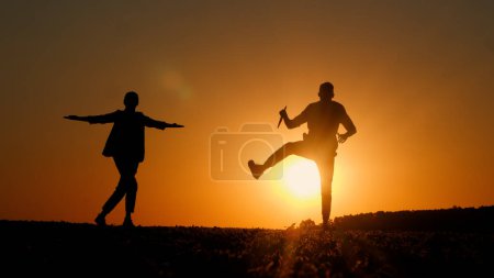 Silhouetten zweier Geschäftsleute, die bei Sonnenuntergang einen fröhlichen Tanz tanzen. Mann hält Tablette in der Hand. 
