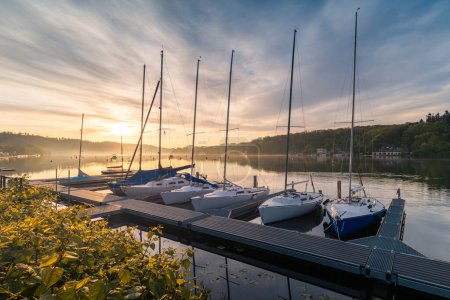 Marina with moored sailboats on Lake Baldeneysee in the city of Essen, beautifully illuminated by the rays of the rising sun.
