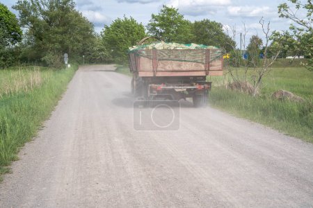 Téléchargez les photos : Tracteur avec une remorque pleine de bois sur un chemin de gravier poussiéreux - en image libre de droit