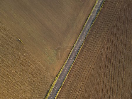 Luftaufnahme von Feldern mit Erde und einer Asphaltstraße in der Mitte