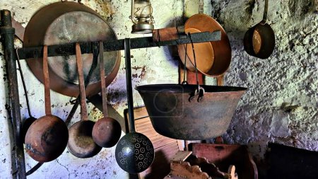 An old tourist pot and ladles on metal plank and two basins on stone wall.