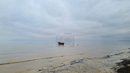 Boat with red flags anchored on calm sea surface against a gray cloudy sky.