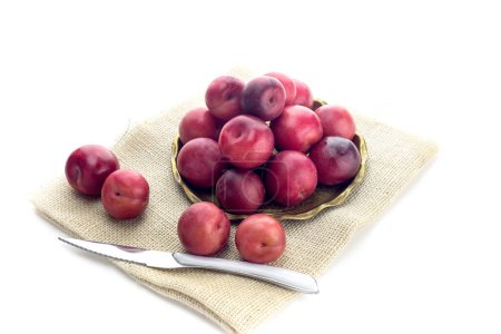 Téléchargez les photos : Des prunes mûres, grosses et douces dans une assiette et un couteau sur fond blanc gros plan - en image libre de droit