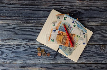 Geschäftsstillleben mit Euro-Scheinen, Münzen, rotem Stift und Notizblock in Großaufnahme auf dem Tisch