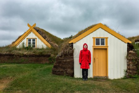 Téléchargez les photos : A girl in a red jacket stands near the peat houses in Iceland .Glaumbaer - en image libre de droit