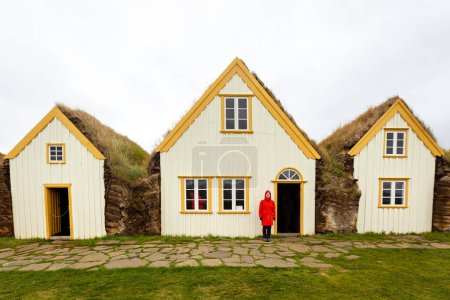 Téléchargez les photos : A girl in a red jacket stands near the peat houses in Iceland .Glaumbaer - en image libre de droit