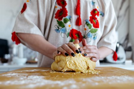 A woman in an embroidered dress kneads dough in the kitchen. Easter holiday. Ukrainian traditions .Selective focus