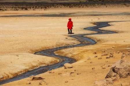 Paysages de l'Islande. Une fille vêtue d'une veste rouge près d'une rivière étroite et ondulée.