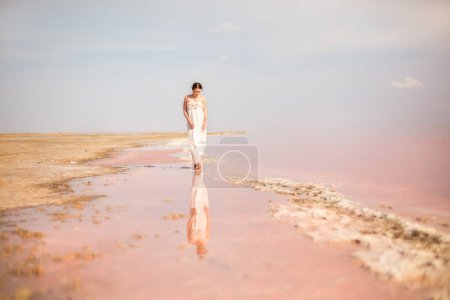 A girl in a white long dress walks on the water of a pink lake. Lemurian lake. Ukraine