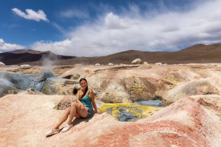 Eine Frau sitzt auf einem Hügel im Hintergrund Sol de Maana Geysire in Bolivien