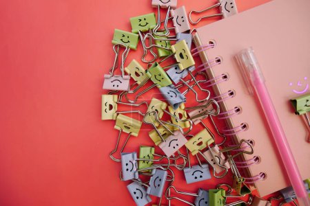 Photo for Pastel colored Office Paper Clips, Smiley Binder Clips, and Pencils on Notepad. Office supplies on aesthetic background. Open spiral notebook on table. Knowledge or education. Back to school - Royalty Free Image