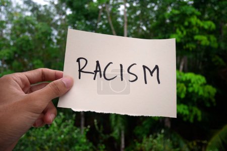 Foto de Libro blanco de mano con texto racista en solitario sobre el fondo de la naturaleza. Concepto de racismo. Discriminación, cuestiones raciales - Imagen libre de derechos