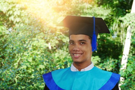 Schöne junge asiatische Absolventin in schwarzem Abschlusskleid und Mütze steht glücklich lächelnd da