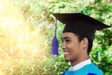 Schöne junge asiatische Absolventin in schwarzem Abschlusskleid und Mütze steht glücklich lächelnd da