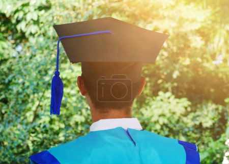Rear view of Asian youth graduating. Students Standing With Graduation Gowns, Caps and Diplomas Against a Background of Nature and Sunlight