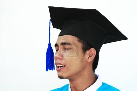 Asiatischer junger Mann mit traurigem Gesicht. Studenten mit Abschlussmänteln, Mützen und Diplomen vor dem Hintergrund von Natur und Sonnenlicht