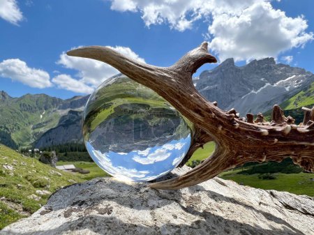 Foto de Impresionantes cuernos de roebuck (trofeo de caza), junto a lente, bola de cristal, reflejos del valle Gauertal (Drei Tuerme, Sulzfluh, Montafon, Vorarlberg). Una de las regiones alpinas de alta montaña más famosas de Austria y los Alpes europeos. - Imagen libre de derechos