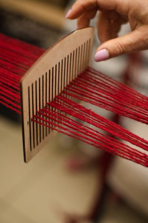 Kunsthandwerker weben bei Tageslicht rote Fäden auf Holzwebstuhl drinnen. Ukrainische kulturelle Authentizität