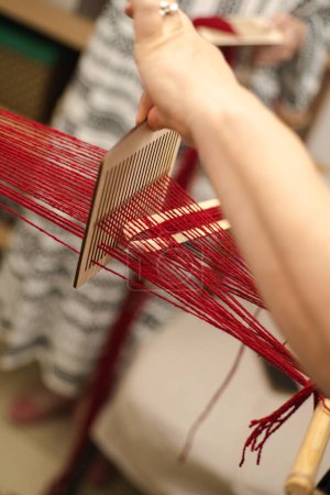 Artisan Weaving Red Thread on Wooden Loom Indoors in Daylight. Ukrainian Cultural authenticity