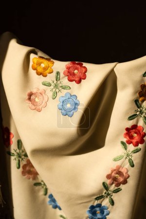 close-up image of white fabric with intricate embroidery featuring colorful flowers and leaves.