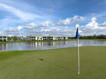 Photo for Golf course green with hole and flag with blue skies and sun. Pristine lush rich green. Southwest Florida. - Royalty Free Image