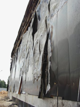 Foto de The facade of a warehouse building made of sandwich panels, which was deformed by a fire. Burnt metal sheets. - Imagen libre de derechos