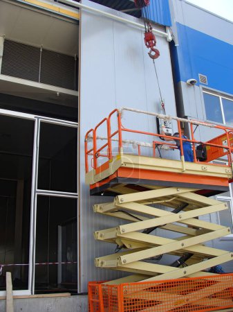 Foto de Trabajador que opera elevadores de tijera, la instalación de paneles de pared utilizando una ventosa. Proceso de construcción de almacén. - Imagen libre de derechos