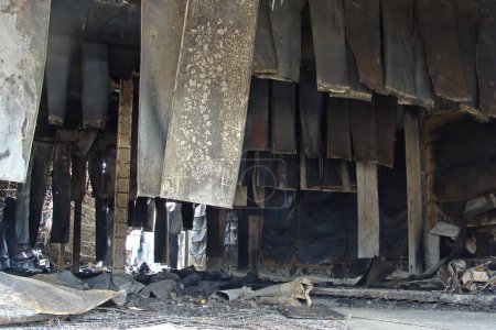 Foto de Después de un incendio en el almacén, las placas de acero carbonizado negro cuelgan del techo como trapos. Incumplimiento de la seguridad contra incendios. - Imagen libre de derechos